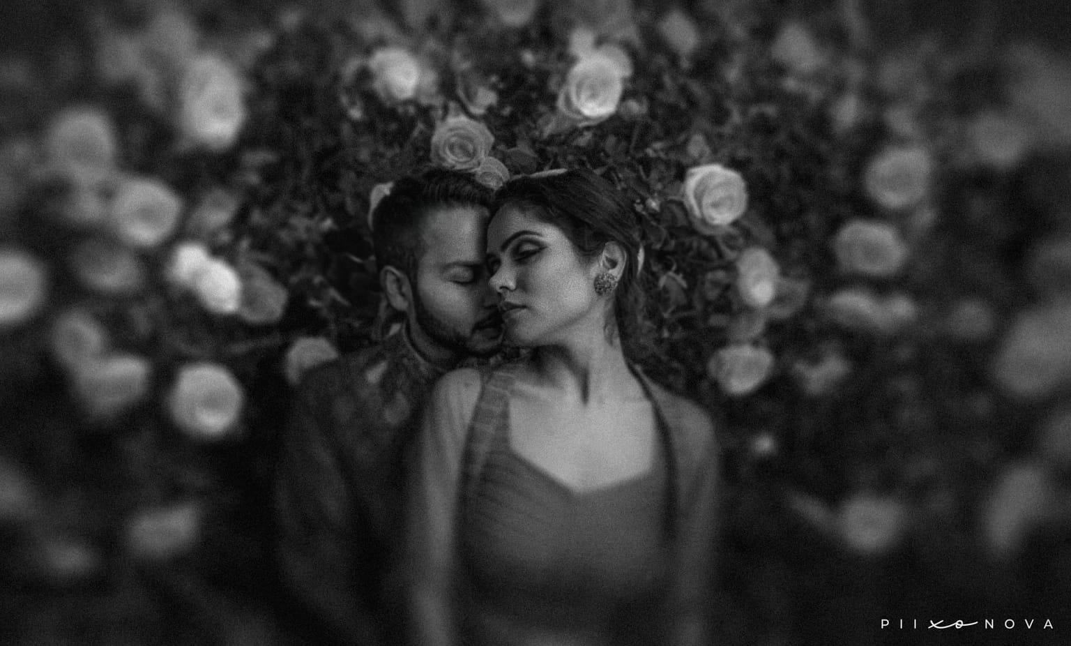 Monochrome artistic pre-wedding portrait of couple lying among blurred rose petals, intimate close embrace, black and white photography, Kolkata