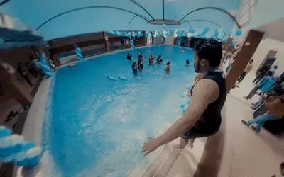 360-degree fisheye shot of indoor pool party with blue and white balloon decorations, guests swimming and celebrating, immersive wedding videography service