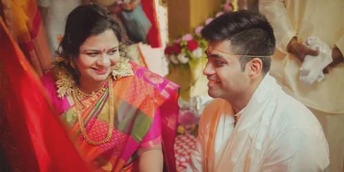 Bride in pink and green traditional silk saree with gold jewelry and mogra flower garland, groom in white kurta with sandalwood tilak, smiling warmly during wedding ritual, Kolkata
